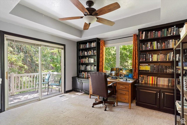 carpeted office space featuring ceiling fan and a tray ceiling