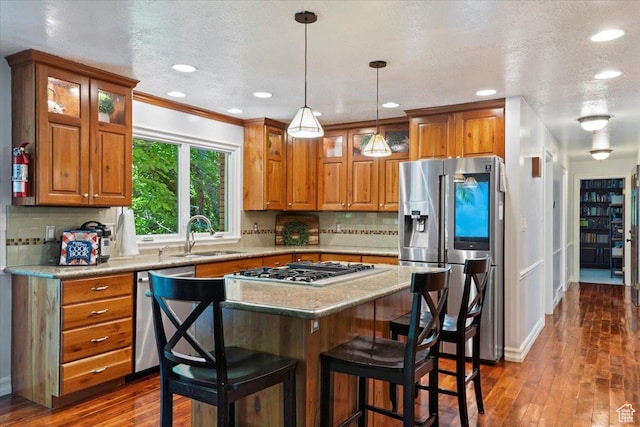 kitchen with sink, a kitchen breakfast bar, backsplash, pendant lighting, and appliances with stainless steel finishes