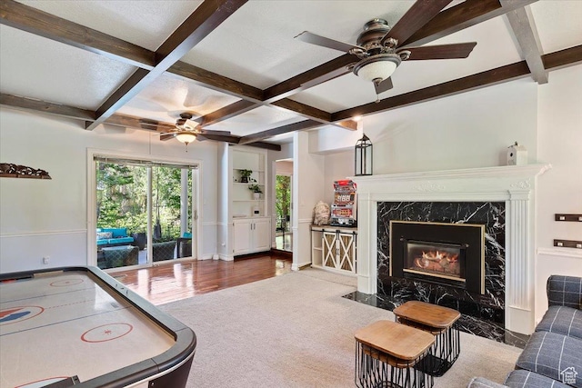 recreation room with beamed ceiling, ceiling fan, a premium fireplace, and coffered ceiling