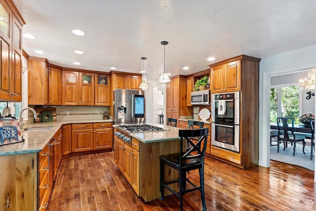 kitchen with sink, a center island, light stone counters, dark hardwood / wood-style floors, and appliances with stainless steel finishes