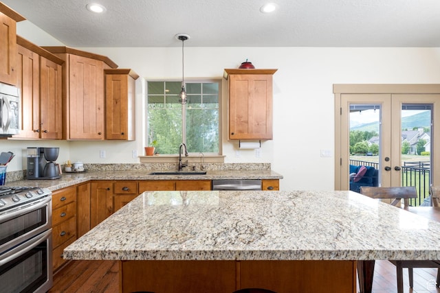 kitchen featuring a kitchen bar, sink, a center island, hanging light fixtures, and stainless steel appliances