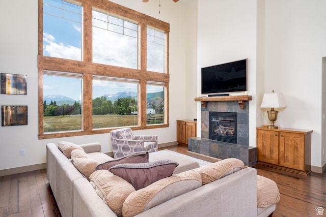 living room featuring dark hardwood / wood-style flooring, a towering ceiling, a tile fireplace, and ceiling fan