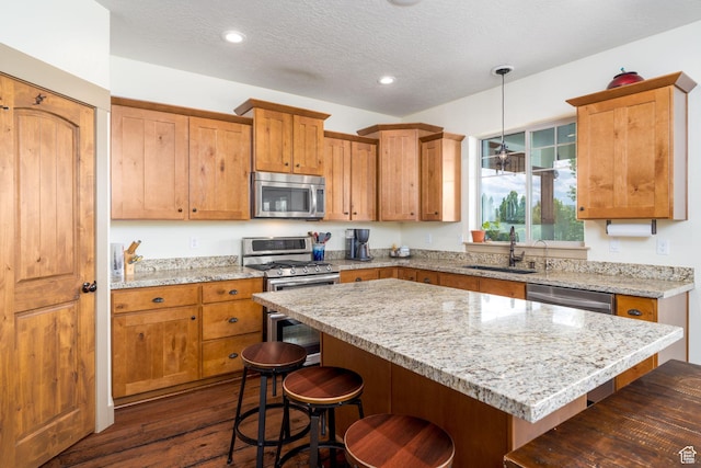 kitchen with a kitchen island, pendant lighting, sink, light stone counters, and stainless steel appliances