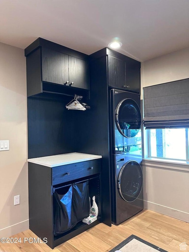 clothes washing area featuring stacked washer and dryer, light hardwood / wood-style floors, and cabinets