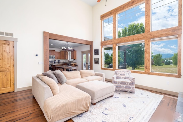living room featuring a high ceiling, wood-type flooring, a healthy amount of sunlight, and ceiling fan with notable chandelier