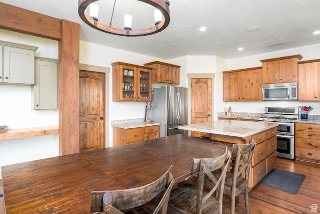 kitchen with a kitchen breakfast bar, a center island, stainless steel appliances, light stone countertops, and dark wood-type flooring