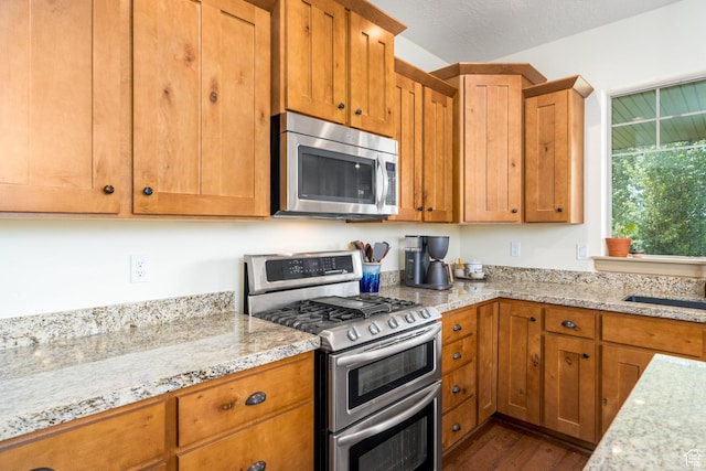 kitchen featuring appliances with stainless steel finishes, hardwood / wood-style floors, sink, light stone countertops, and a textured ceiling