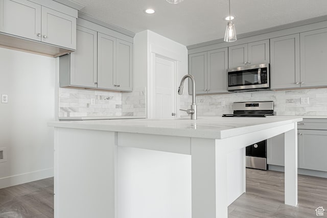 kitchen with backsplash, stainless steel appliances, a center island with sink, and gray cabinetry