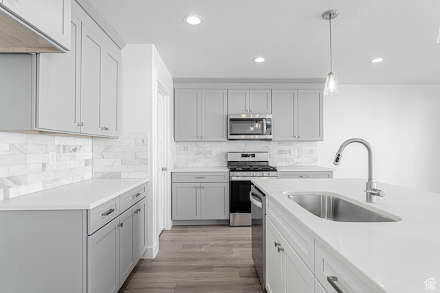 kitchen featuring appliances with stainless steel finishes, sink, decorative light fixtures, light hardwood / wood-style flooring, and gray cabinets