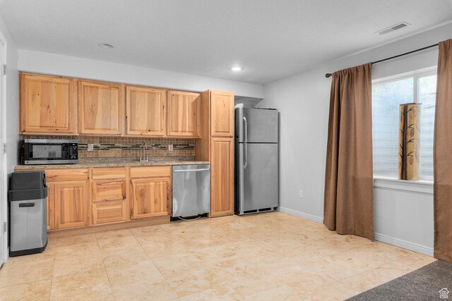 kitchen featuring visible vents, a sink, backsplash, appliances with stainless steel finishes, and baseboards