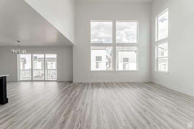 3772 W 1200 N Unit 135, Lehi, UT 84043 - unfurnished living room with a chandelier, light wood-style flooring, healthy amount of natural light, baseboards, and a high ceiling