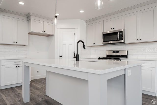 kitchen with sink, appliances with stainless steel finishes, a kitchen island with sink, hanging light fixtures, and white cabinets