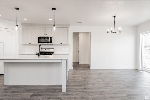 kitchen with decorative light fixtures, appliances with stainless steel finishes, a healthy amount of sunlight, a kitchen island with sink, and white cabinets