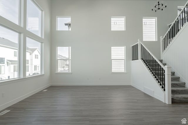unfurnished living room featuring a notable chandelier, dark hardwood / wood-style flooring, and a towering ceiling