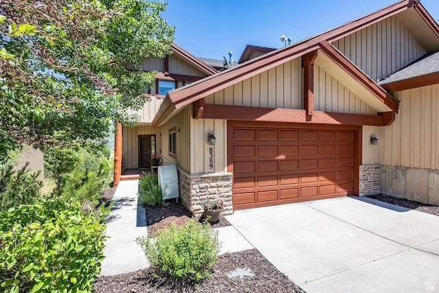 view of front of house with stone siding, an attached garage, board and batten siding, and driveway