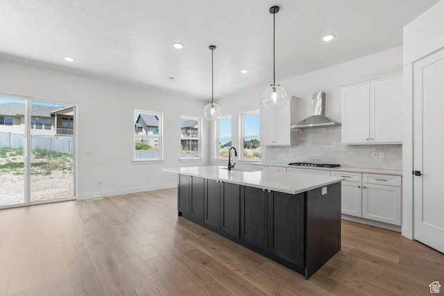 kitchen with a sink, light countertops, wall chimney exhaust hood, and white cabinets