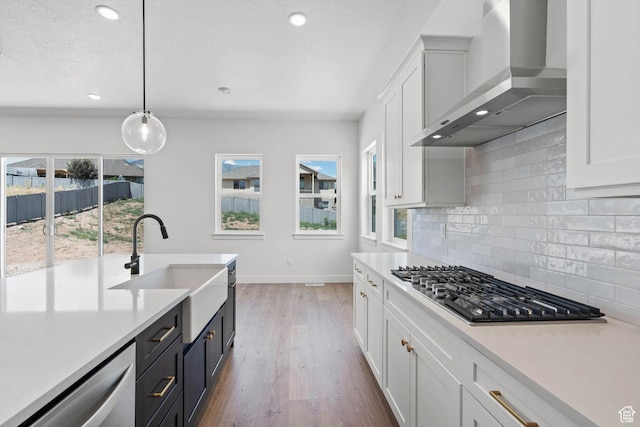 kitchen with wall chimney range hood, stainless steel appliances, light countertops, and white cabinetry