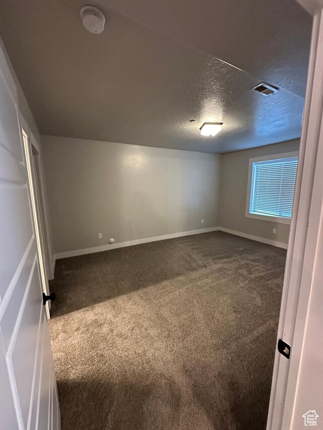 unfurnished bedroom featuring a textured ceiling, dark colored carpet, baseboards, and visible vents
