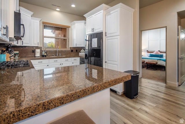 kitchen featuring white cabinetry, black refrigerator, light hardwood / wood-style floors, stainless steel gas cooktop, and kitchen peninsula