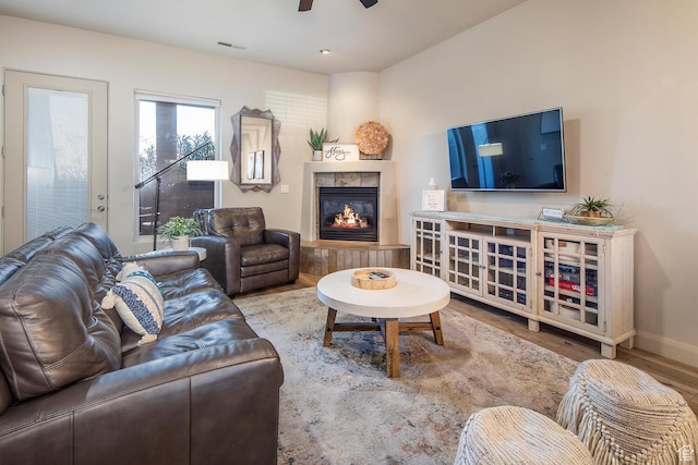 living room with a tile fireplace, wood-type flooring, and ceiling fan
