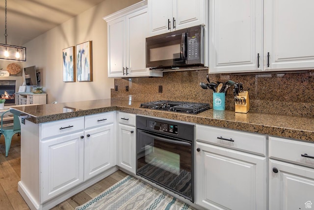 kitchen featuring black appliances, hanging light fixtures, kitchen peninsula, white cabinets, and backsplash