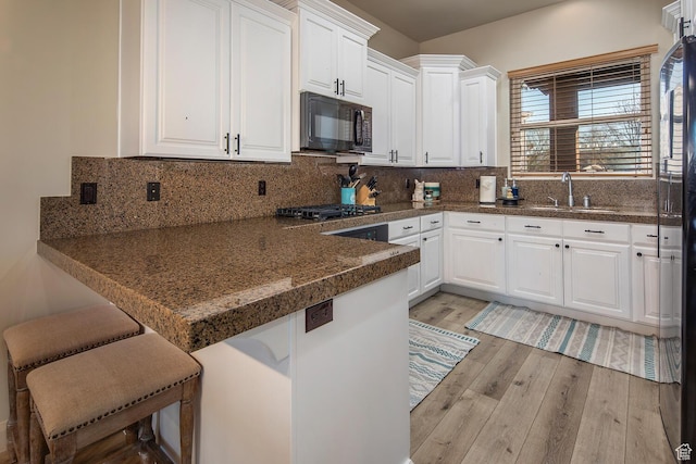 kitchen with a kitchen bar, sink, white cabinetry, tasteful backsplash, and light wood-type flooring
