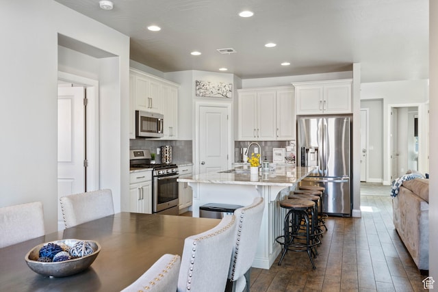 kitchen with stainless steel appliances, visible vents, decorative backsplash, white cabinets, and a sink