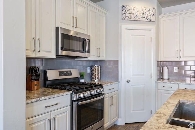 kitchen featuring appliances with stainless steel finishes, light stone countertops, white cabinetry, and tasteful backsplash