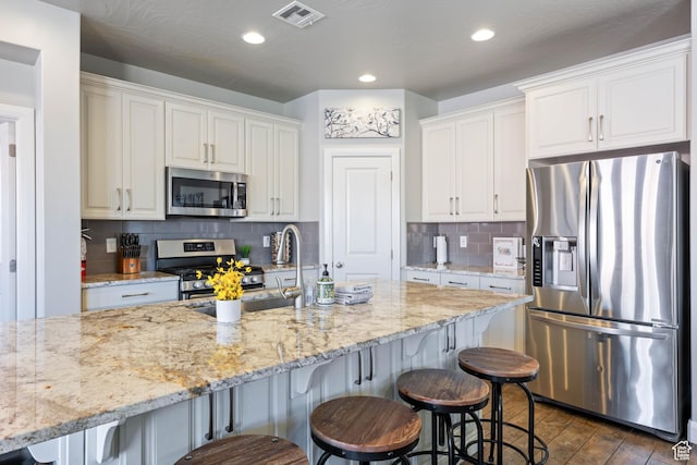 kitchen featuring visible vents, a breakfast bar, light stone countertops, stainless steel appliances, and white cabinetry
