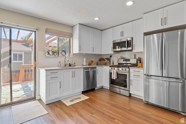 kitchen with sink, light hardwood / wood-style floors, a textured ceiling, white cabinets, and appliances with stainless steel finishes
