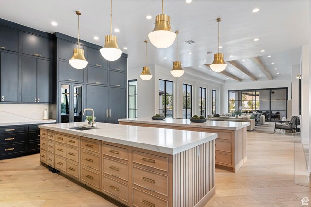 3905 S Quarry Ridge Dr, St George, UT 84790 - kitchen featuring light stone counters, hanging light fixtures, a center island with sink, light brown cabinets, and light hardwood / wood-style floors
