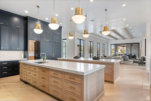 3905 S Quarry Ridge Dr, St George, UT 84790 - kitchen with light brown cabinetry, light stone counters, hanging light fixtures, an island with sink, and light hardwood / wood-style floors