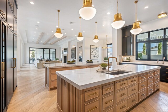 3905 S Quarry Ridge Dr, St George, UT 84790 - kitchen featuring decorative light fixtures, sink, light hardwood / wood-style floors, light stone countertops, and a center island with sink