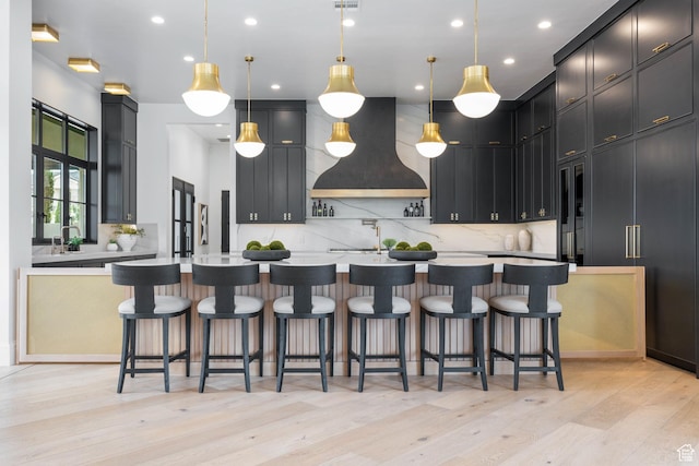 3905 S Quarry Ridge Dr, St George, UT 84790 - kitchen with decorative light fixtures, tasteful backsplash, custom exhaust hood, a large island, and light hardwood / wood-style floors