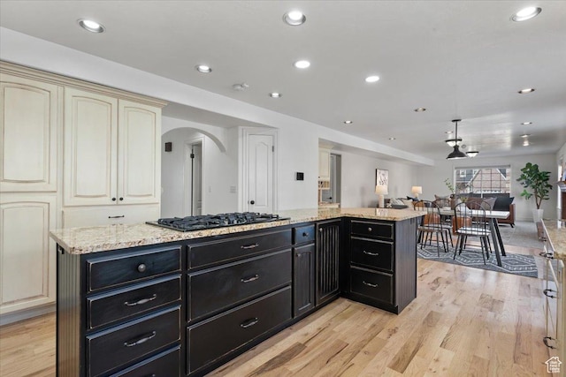 kitchen featuring dark cabinetry, arched walkways, cream cabinetry, black gas stovetop, and open floor plan