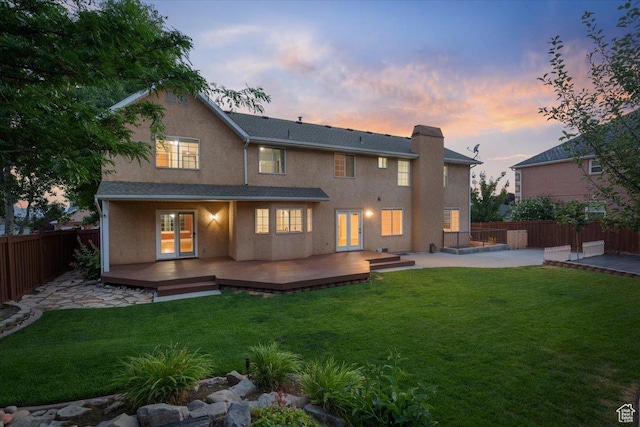 rear view of house with a fenced backyard, a chimney, stucco siding, a deck, and a lawn