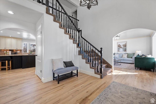 stairs featuring arched walkways, a high ceiling, baseboards, and wood finished floors