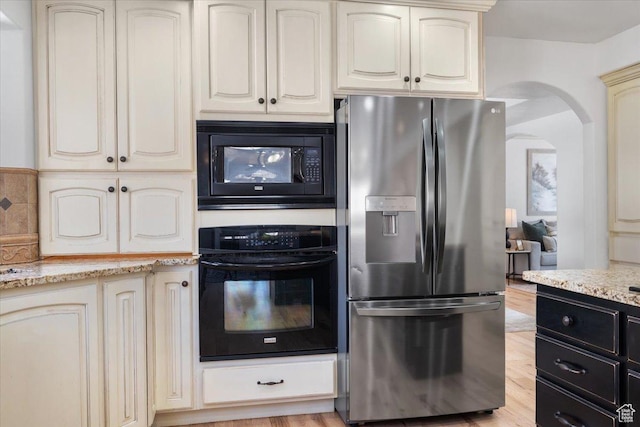 kitchen featuring arched walkways, cream cabinetry, black appliances, and light wood-style floors