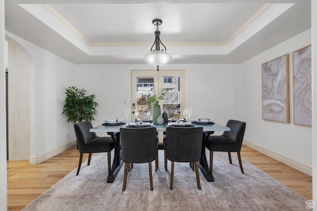 dining area with a raised ceiling, crown molding, and light wood-type flooring