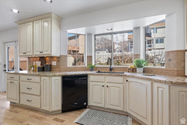 kitchen with light wood finished floors, black dishwasher, decorative backsplash, cream cabinetry, and a sink