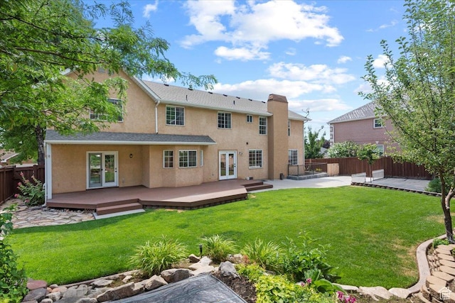 rear view of property with stucco siding, french doors, a lawn, a deck, and a fenced backyard