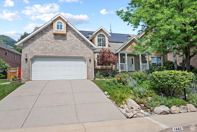 view of front facade featuring driveway, roof mounted solar panels, a porch, a garage, and brick siding