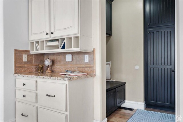 interior space featuring open shelves, tasteful backsplash, white cabinets, light wood finished floors, and light stone countertops