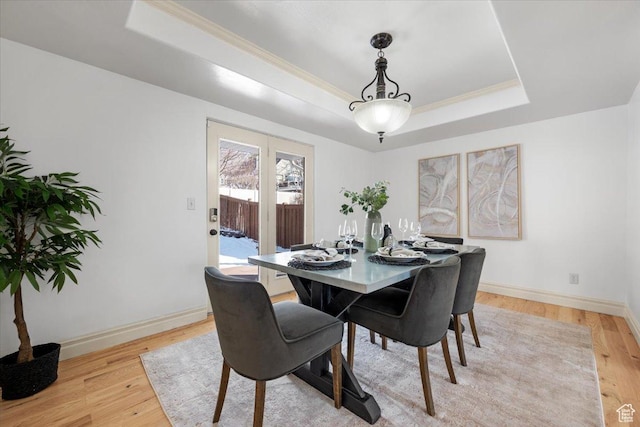 dining room featuring light wood-type flooring, a raised ceiling, baseboards, and crown molding