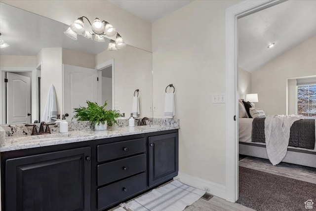 full bath with baseboards, double vanity, a sink, vaulted ceiling, and ensuite bathroom