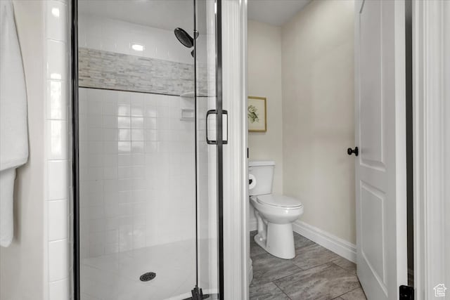bathroom with a shower stall, toilet, and baseboards