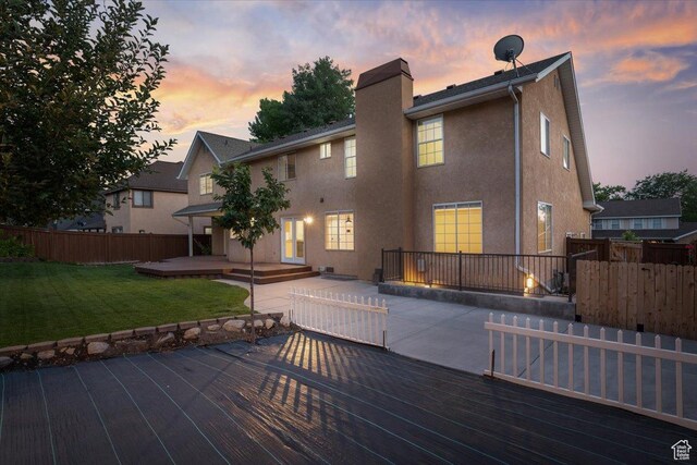back of house at dusk with fence, stucco siding, a lawn, a chimney, and a patio area