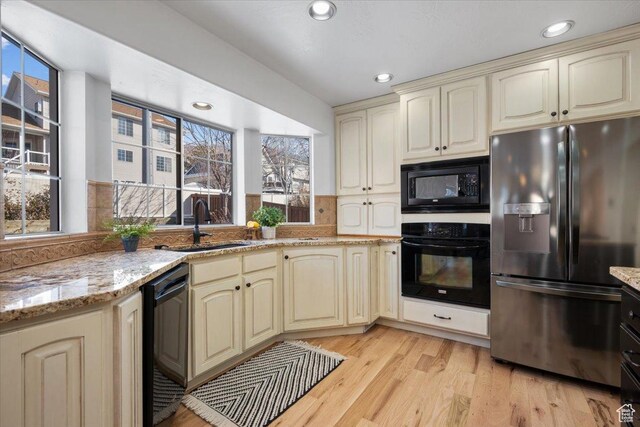 kitchen featuring cream cabinetry, black appliances, light wood-type flooring, and a sink