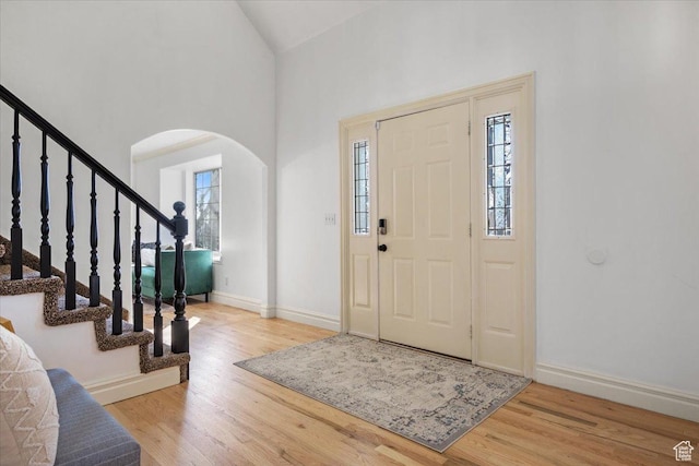 entryway featuring arched walkways, stairway, baseboards, and wood finished floors