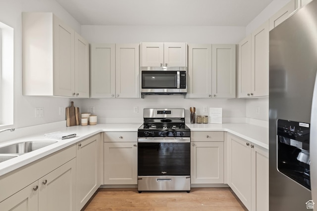 kitchen with light countertops, a sink, stainless steel appliances, and light wood-type flooring